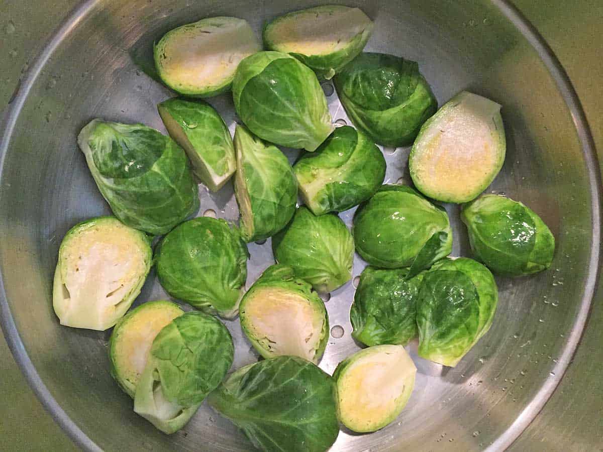 A pound of halved Brussel sprouts in a stainless steel steamer basket