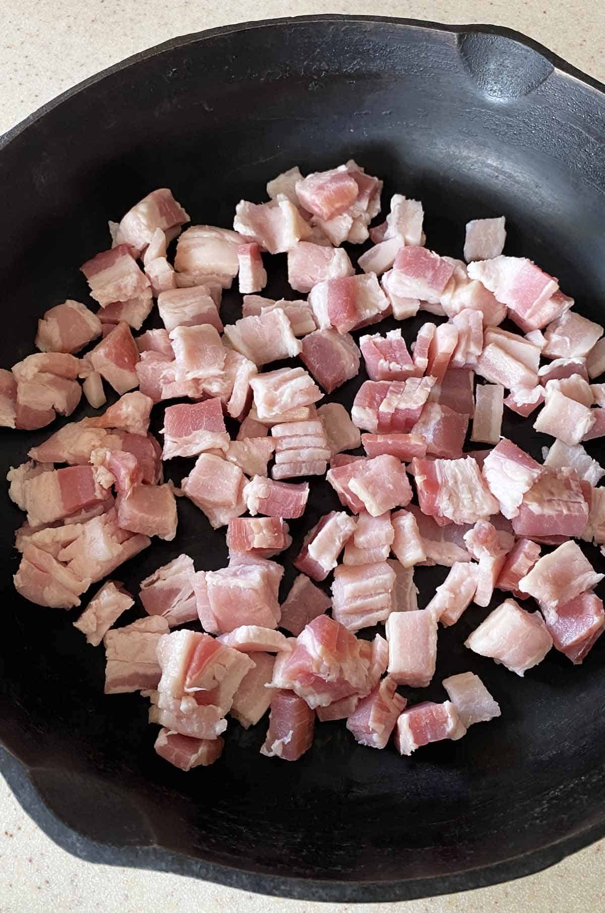 Close up image of 8 slices of chopped bacon in a black cast iron skillet