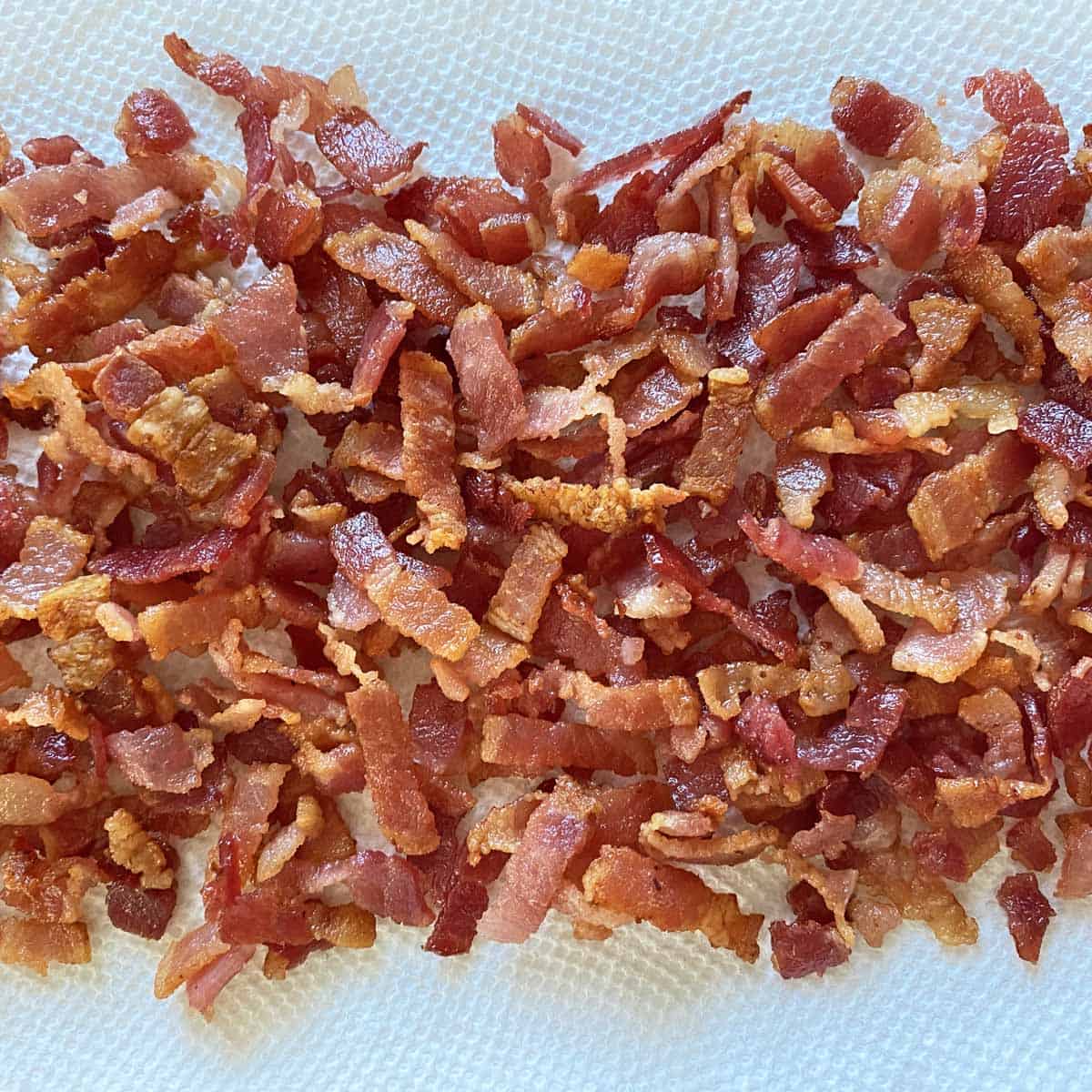 Cooked bacon strips draining on white paper towels