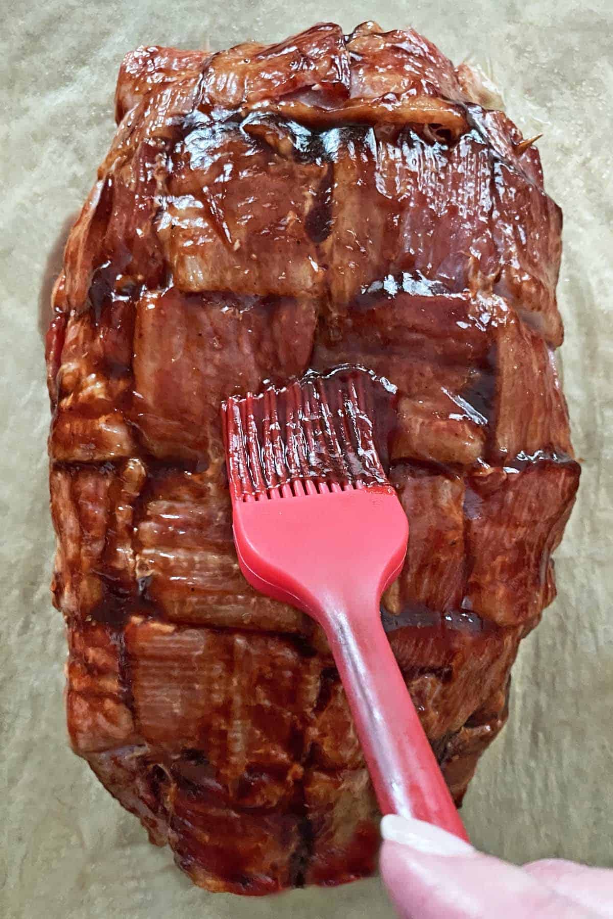 A red silicone brush basting the bacon weave meatloaf with barbecue sauce