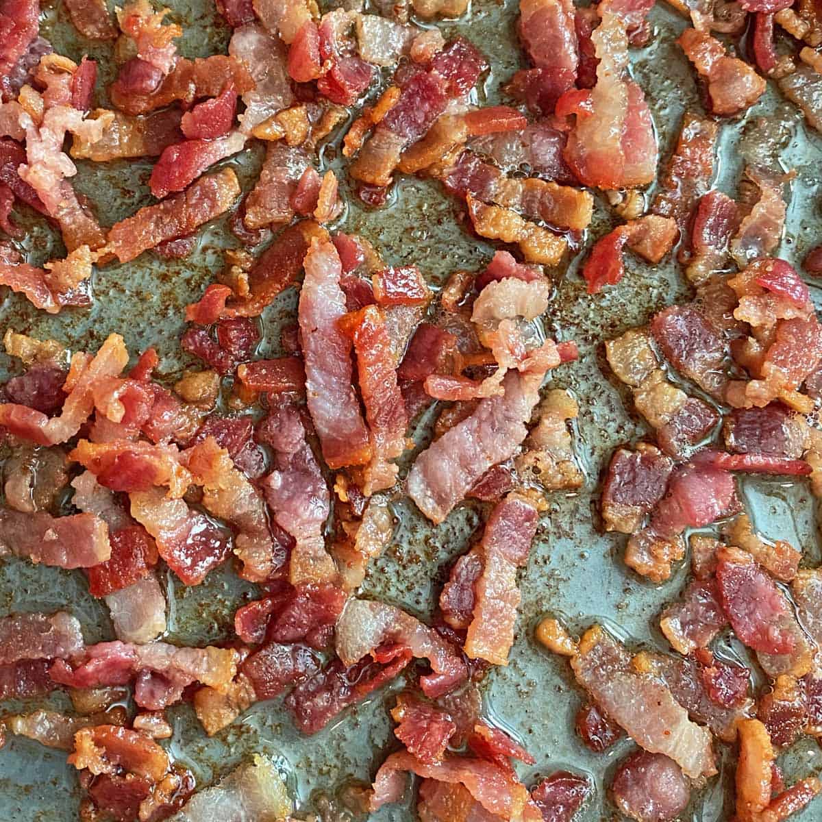 Close up of bacon strips cooking in a large skillet. 