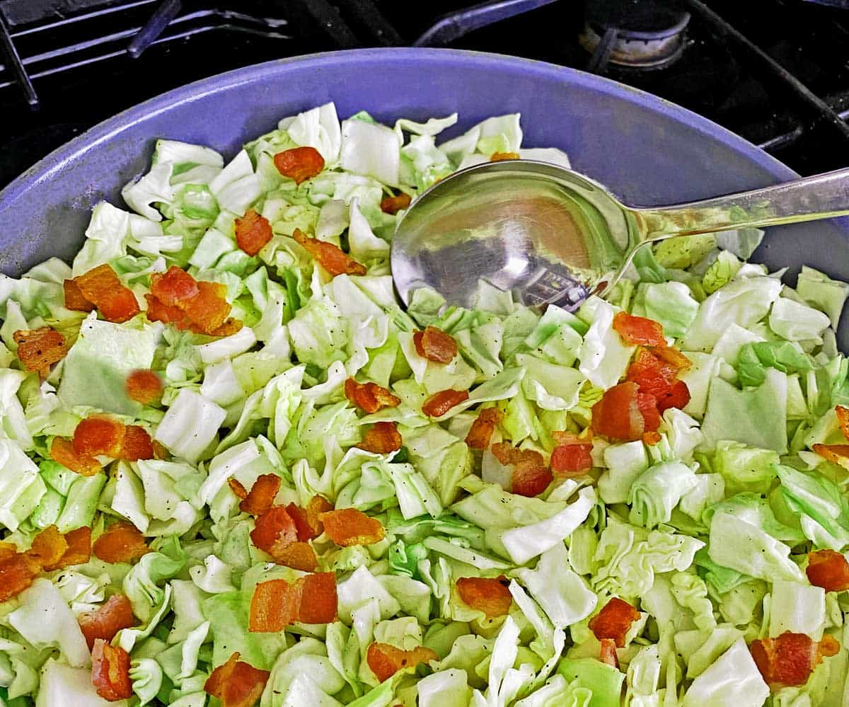 Close up of skillet with partially cooked cabbage and bacon.