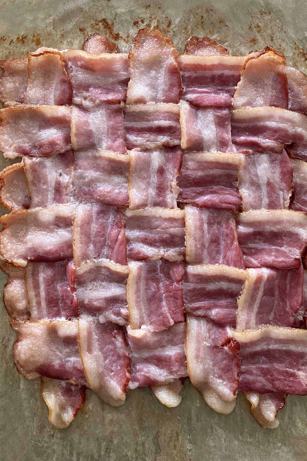 A close up of a partially cooked bacon weave on a piece of parchment paper