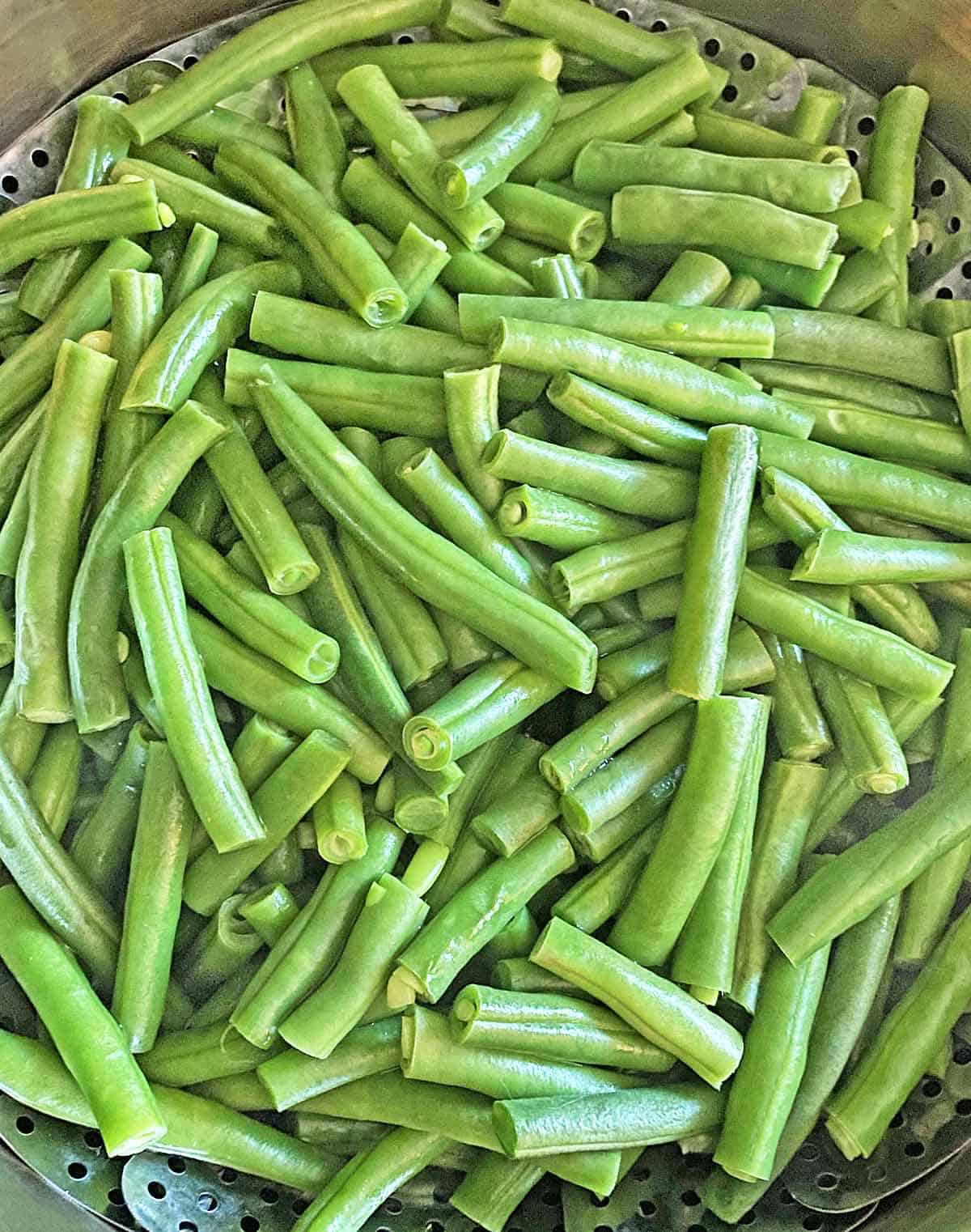 Steamed green beans in a silver steamer basket.
