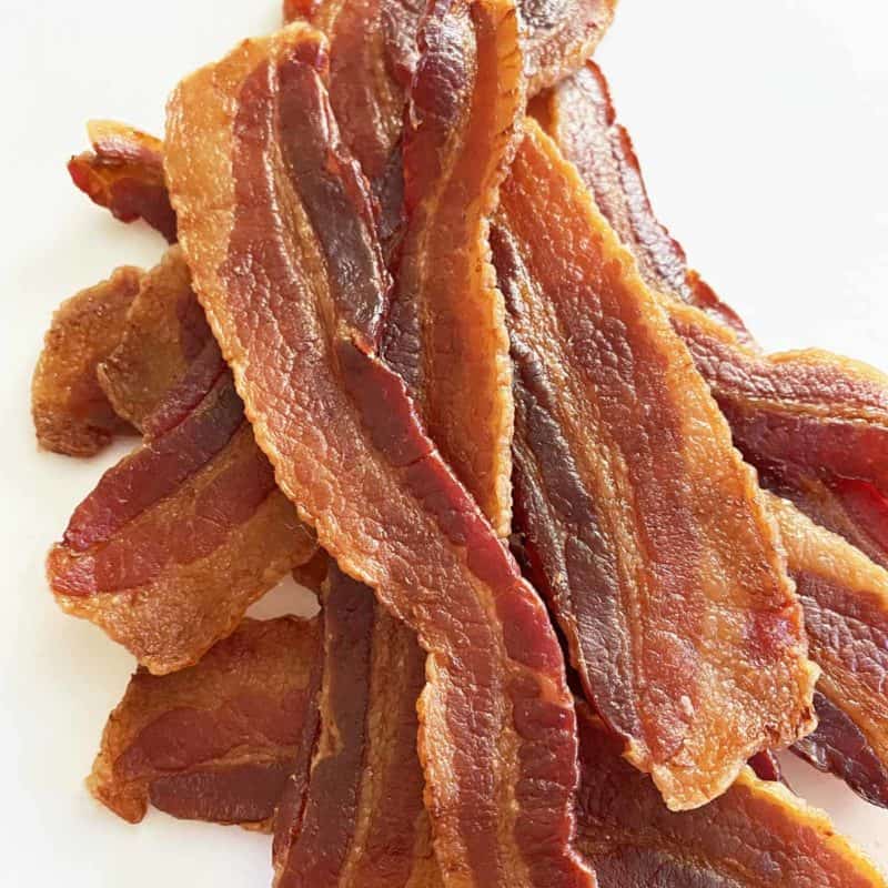 A dozen strips of homemade bacon jerky in a pile on a white background