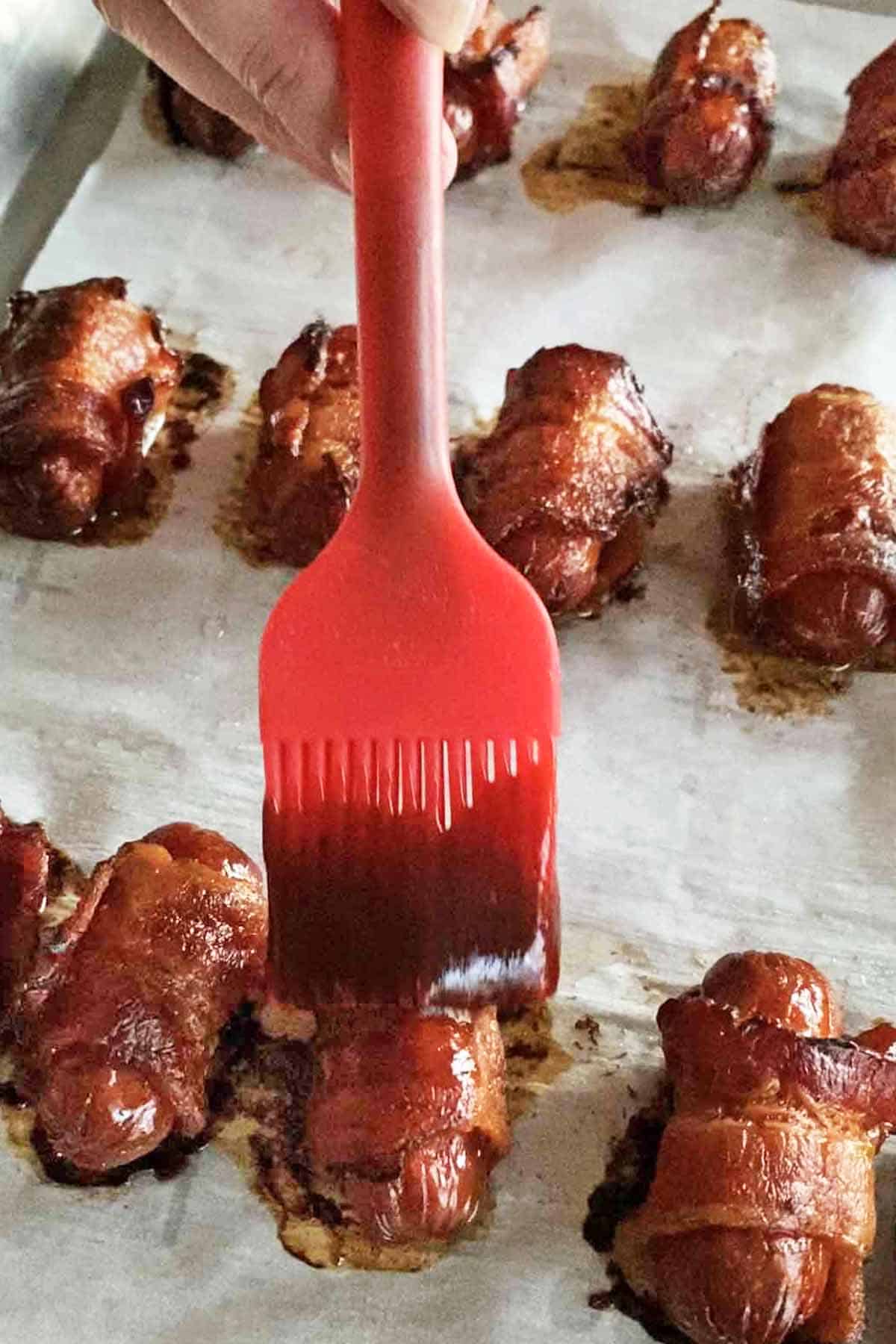 close up of glazing bacon wrapped smokies with BBQ sauce using a red silicone basting brush
