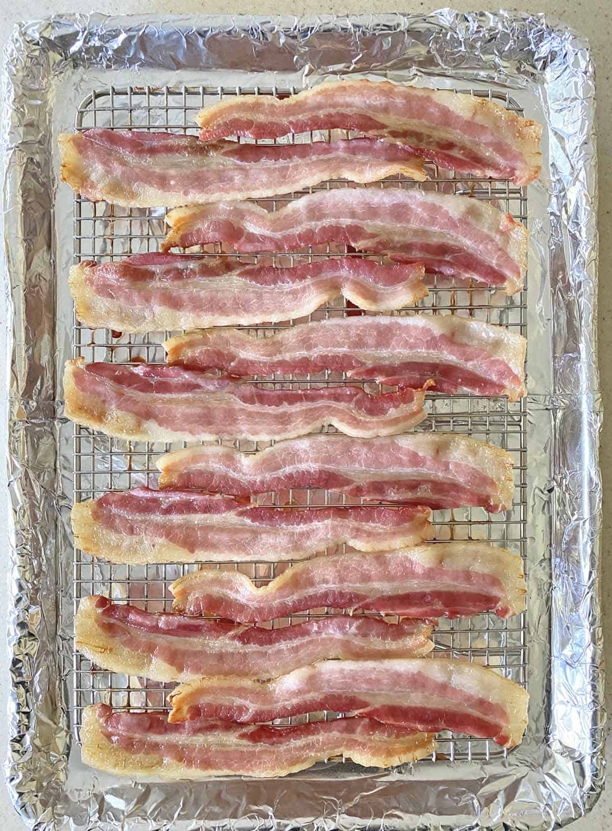 12 slices of partially cooked bacon jerky on a baking rack set on a foil lined baking sheet.