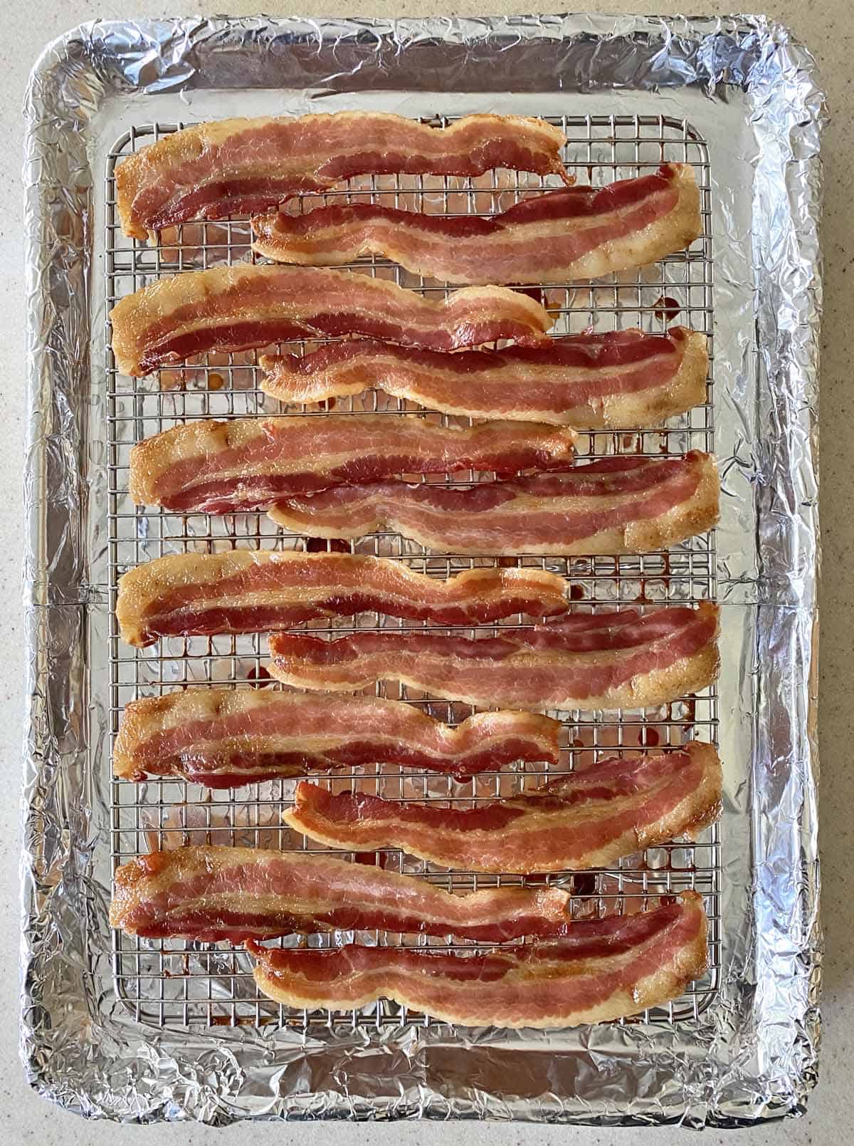 12 slices of half-cooked bacon jerky on a baking pan lined with foil and topped with a wire baking rack. 