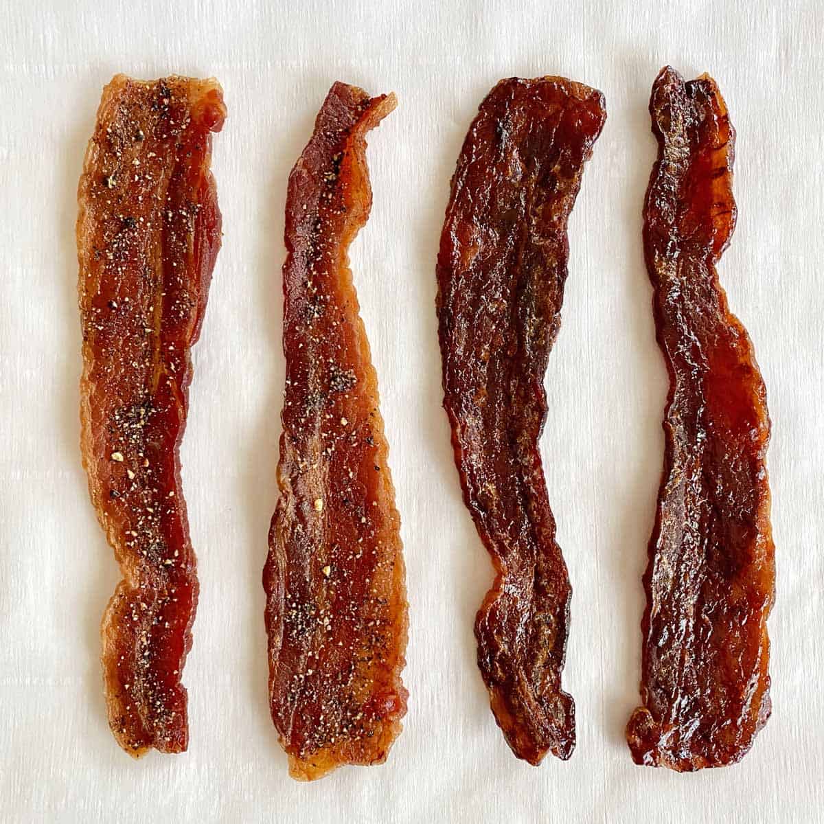 Two strips of black pepper bacon jerky and two strips of barbecue bacon jerky on a piece of white parchment paper