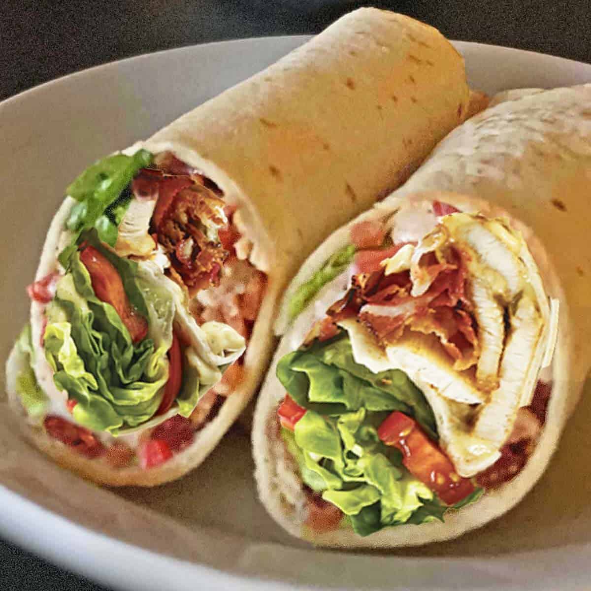 Close up of chicken bacon ranch wrap sandwich cut in half on a white plate.