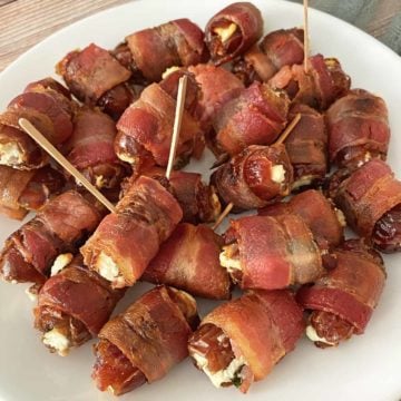 Thirty cooked bacon wrapped dates stuffed with goat cheese on a white plate.