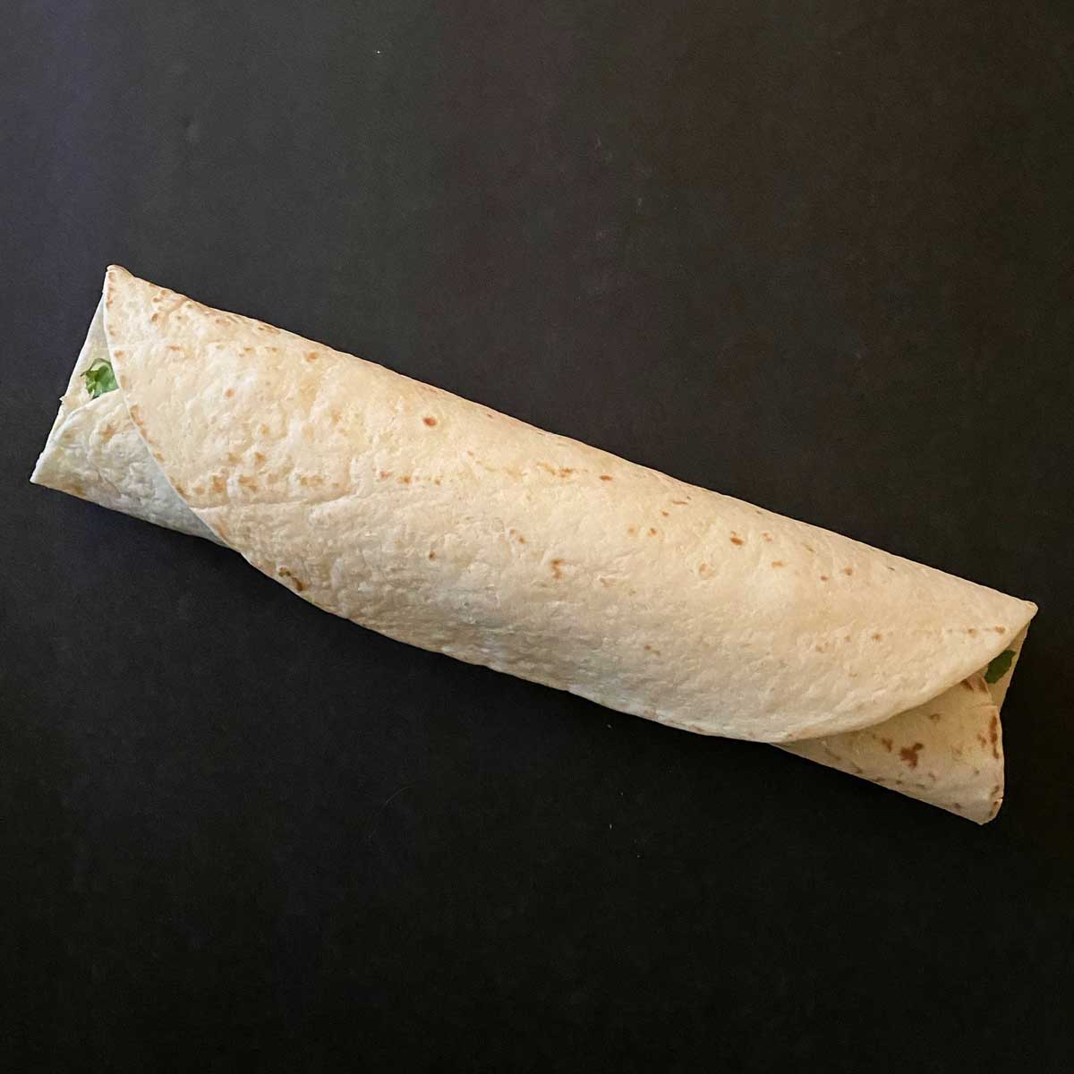 A large flour tortilla tightly wrapped around the chicken bacon filling.