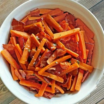 White serving dish filled with carrots and bacon with maple syrup
