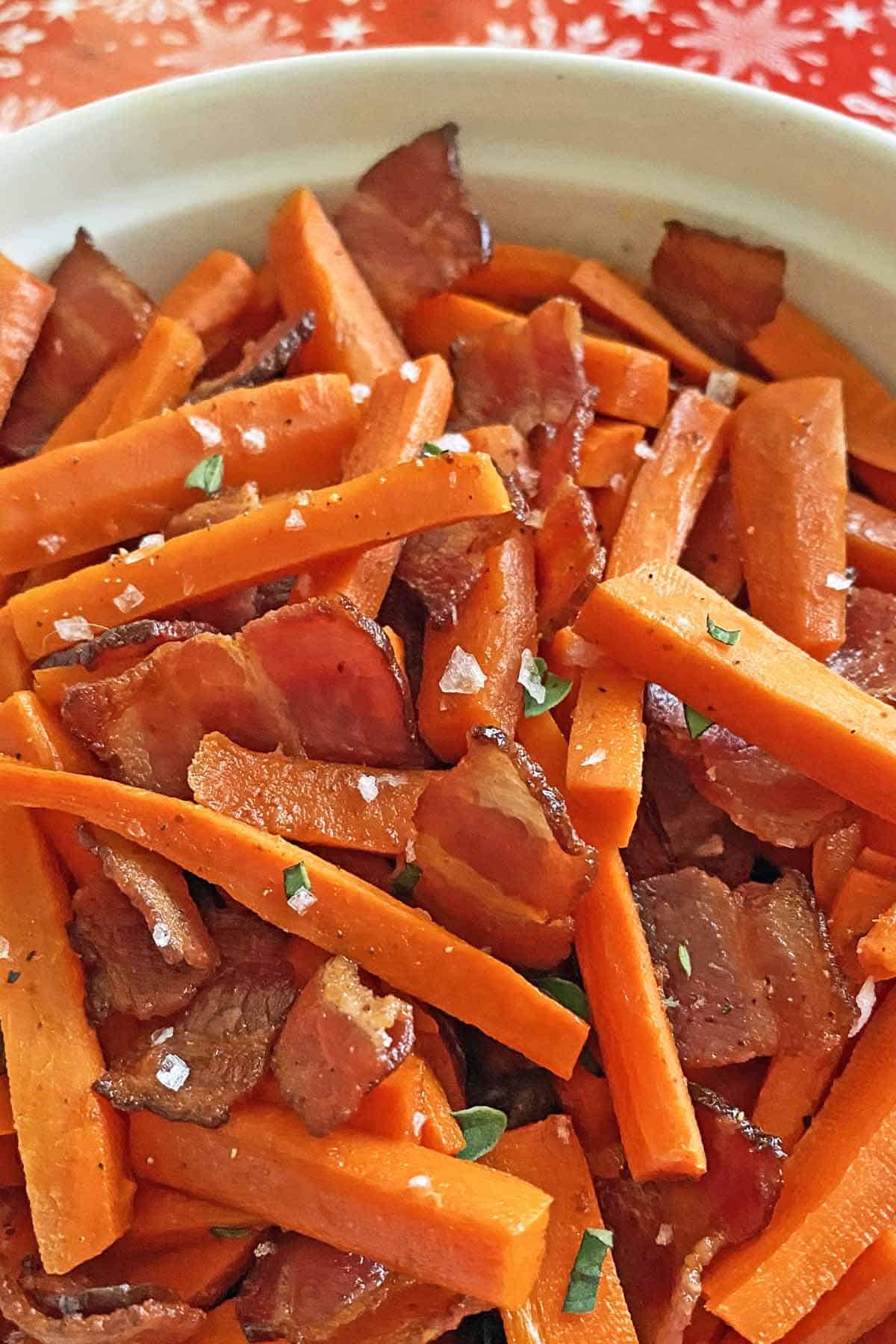 Close up of white dish filled with carrots and bacon with maple syrup.