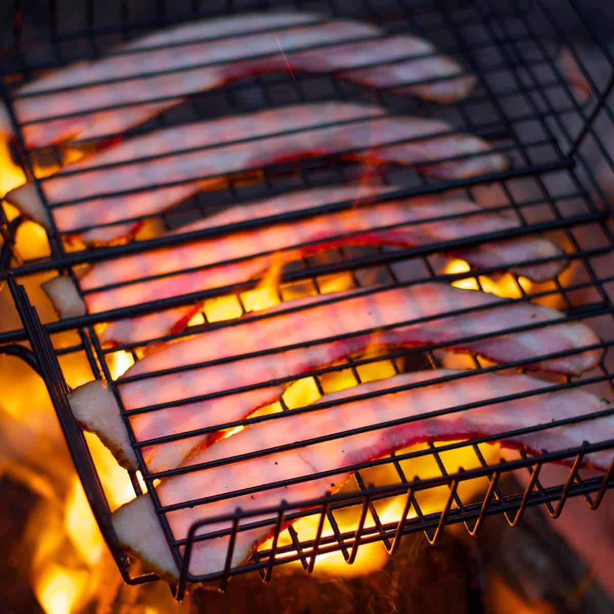 5 strips of thick cut bacon being grilled over an open flame. 