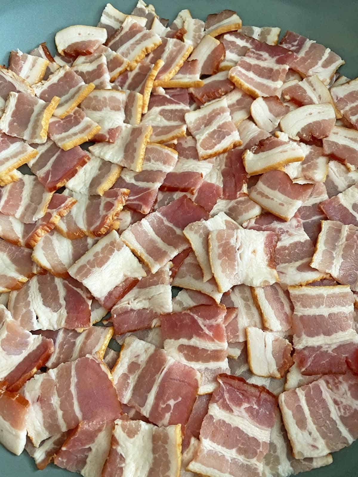 A pile of cut bacon pieces in a gray skillet.