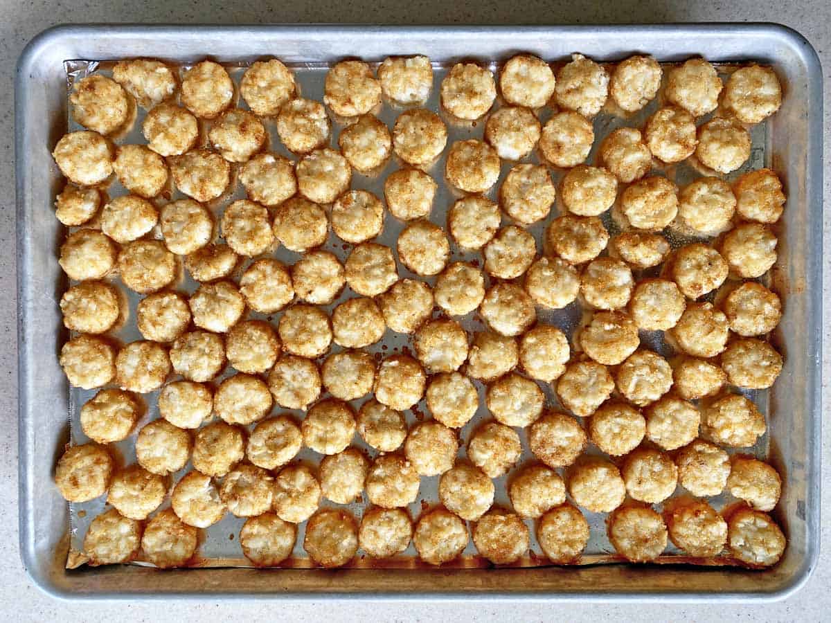 Frozen tater tots spread on a large baking sheet.