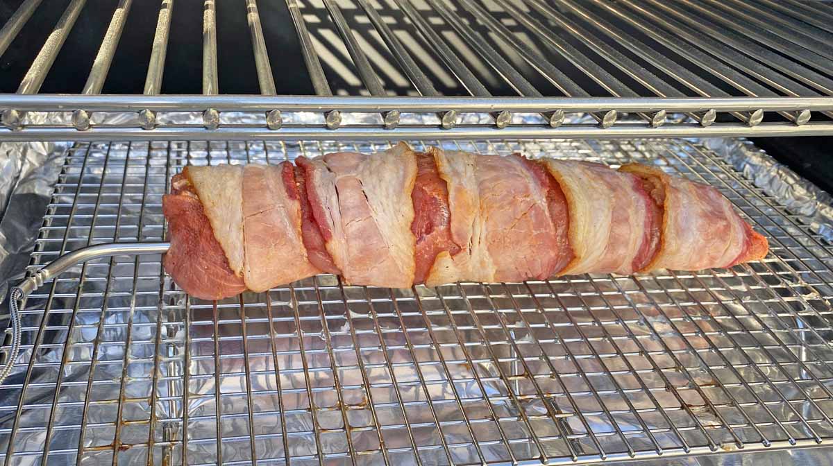 Bacon wrapped pork tenderloin in the smoker, with a temperature probe inserted in the left end. 