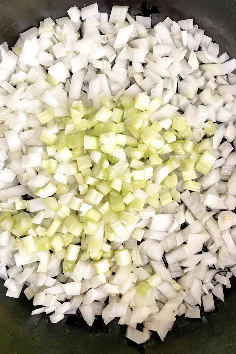 Chopped onions and celery cooking in a cast iron skillet.