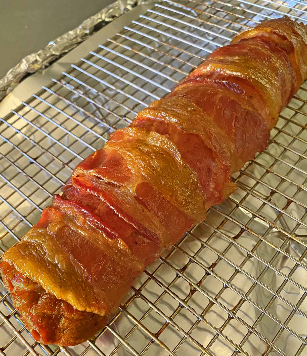 Just cooked, bacon-wrapped pork tenderloin is shown on a baking sheet after being pulled from the smoker.