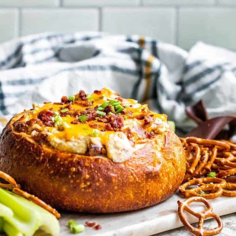 Game day cheese dip with bacon in a bread bowl with pretzels
