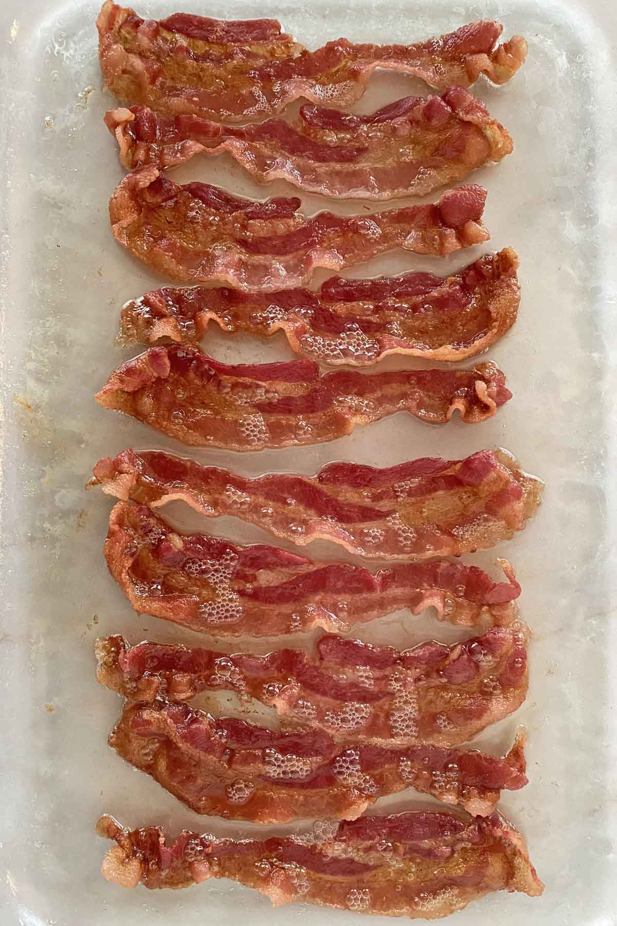 Ten strips of golden brown cooked bacon in a glass baking dish. 