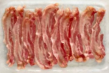 10 strips of partially cooked bacon in a glass baking dish.