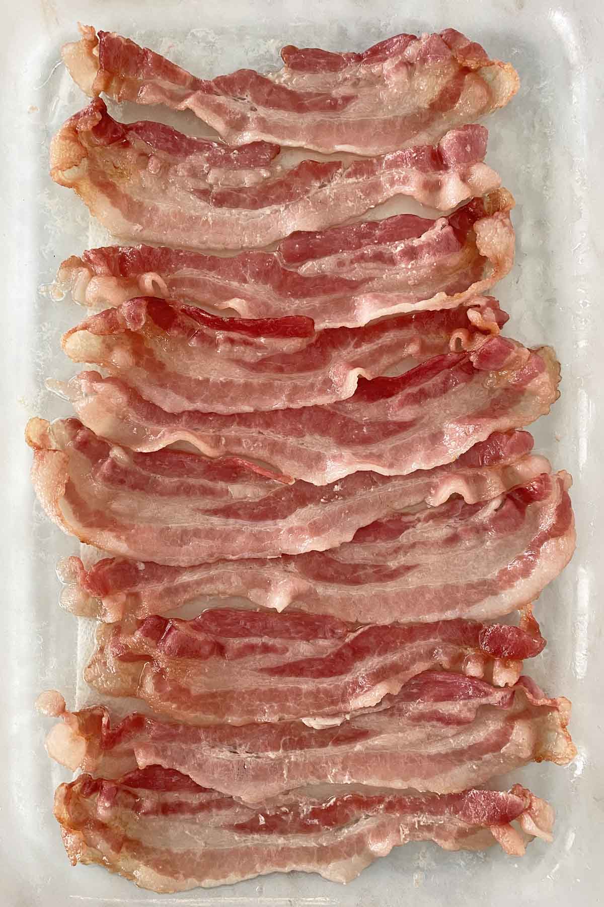 10 strips of partially cooked microwave bacon in a glass baking dish.