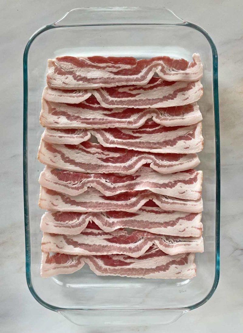 10 strips of uncooked thick sliced bacon in a glass baking dish.