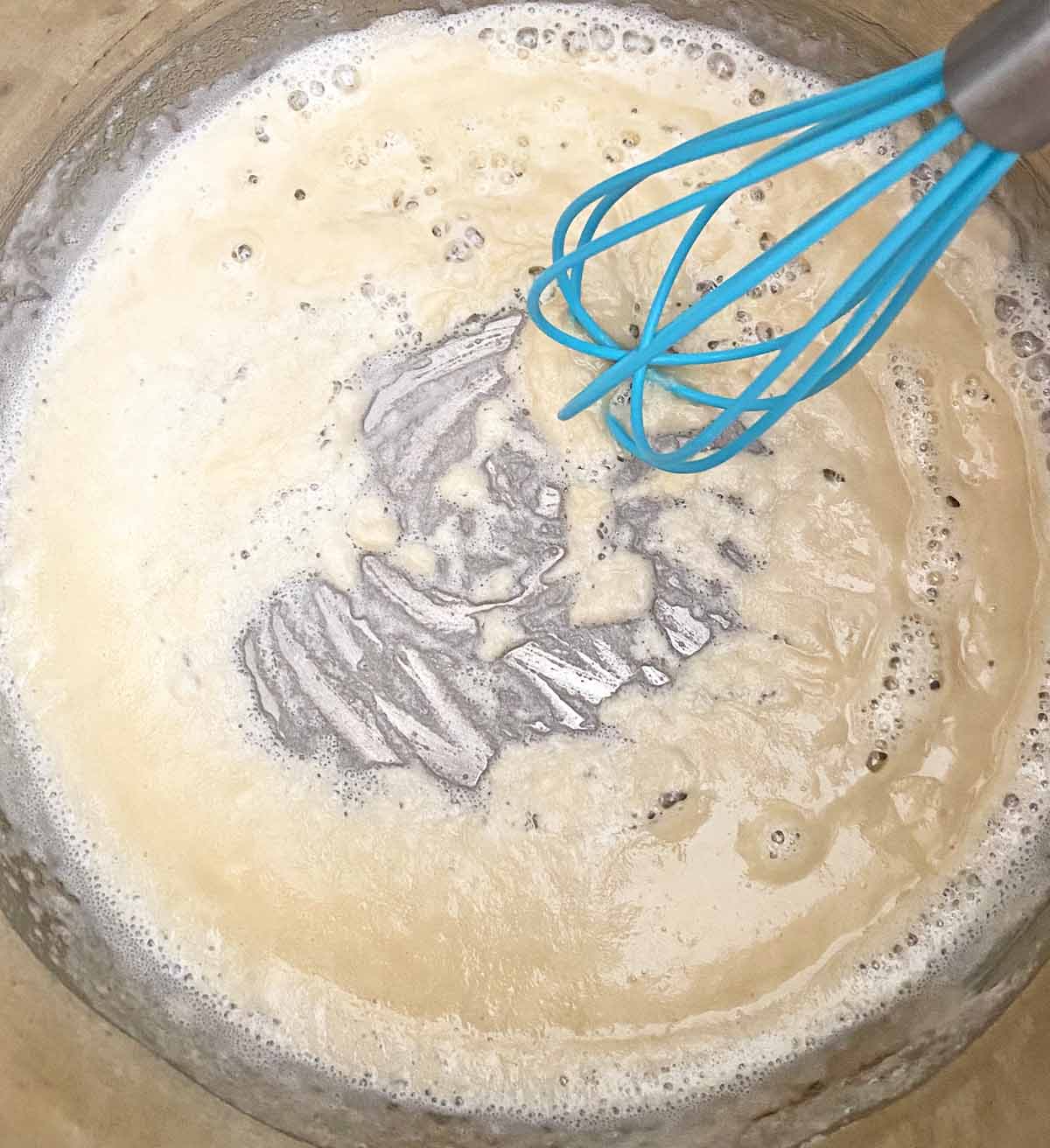 A blue whisk and the flour, butter and bacon grease mixture cooking in a pot.