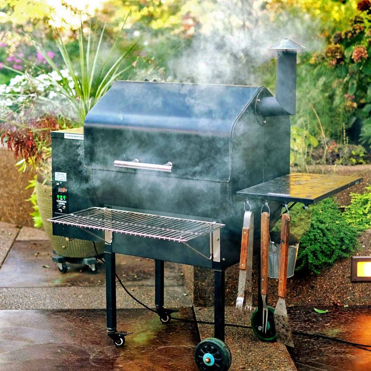 A hot smoker grill with smoke wafting around it, set in a pretty garden patio area.