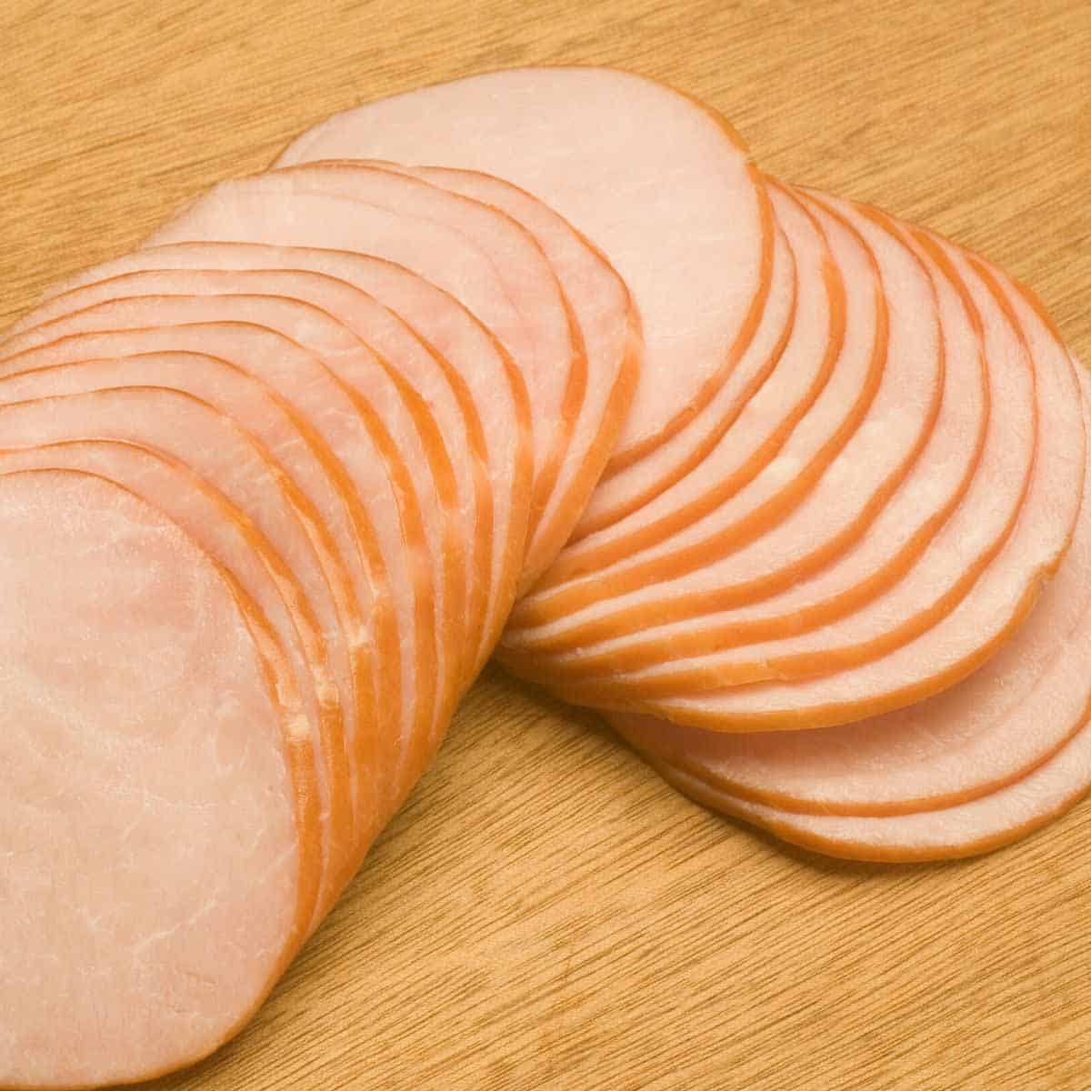 Sliced rounds of Canadian bacon on a wooden cutting board.