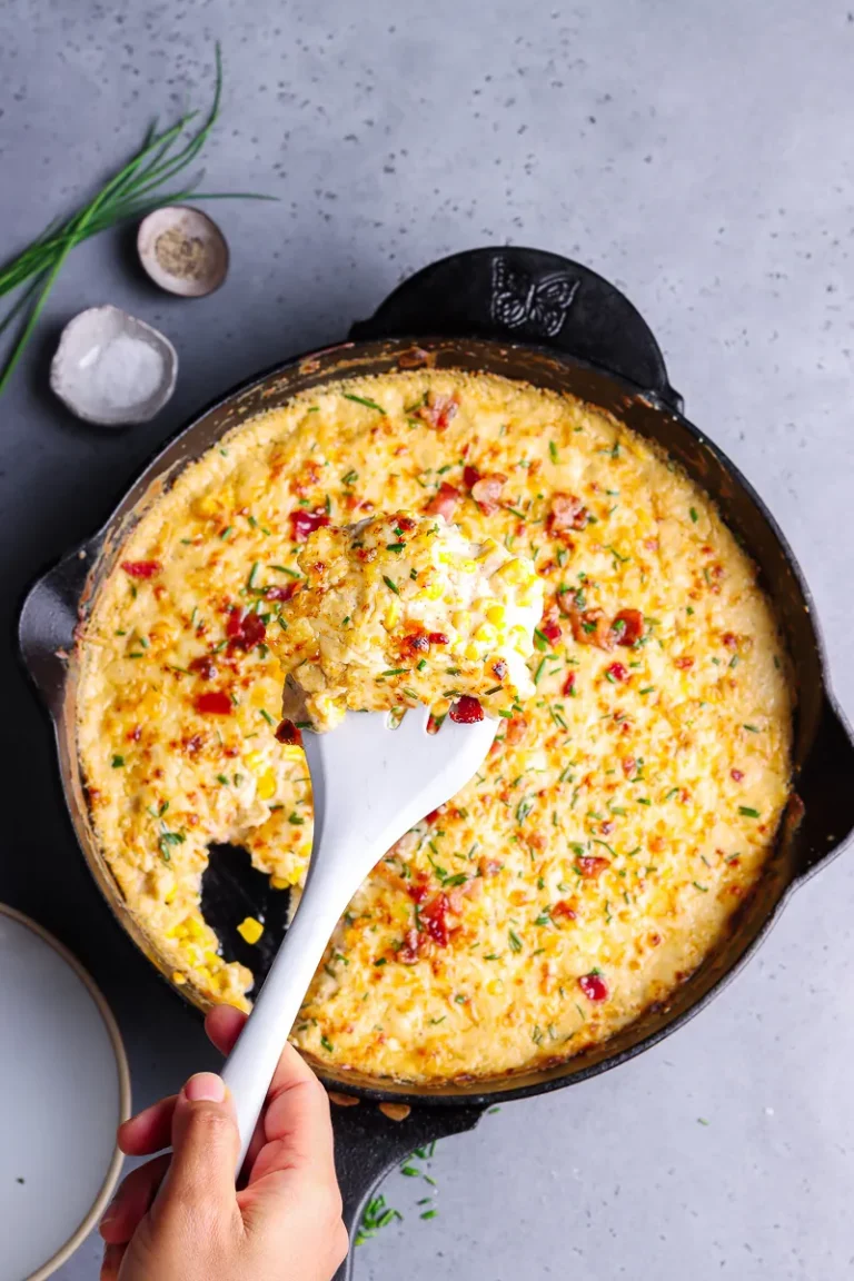 Cheesy corn casserole with bacon in a black cast iron skillet with a white spoon.