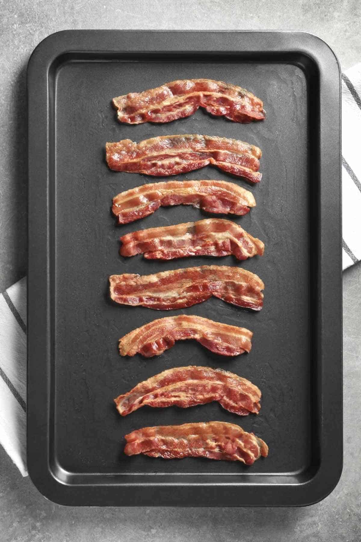 8 strips of cooked bacon on a baking sheet.