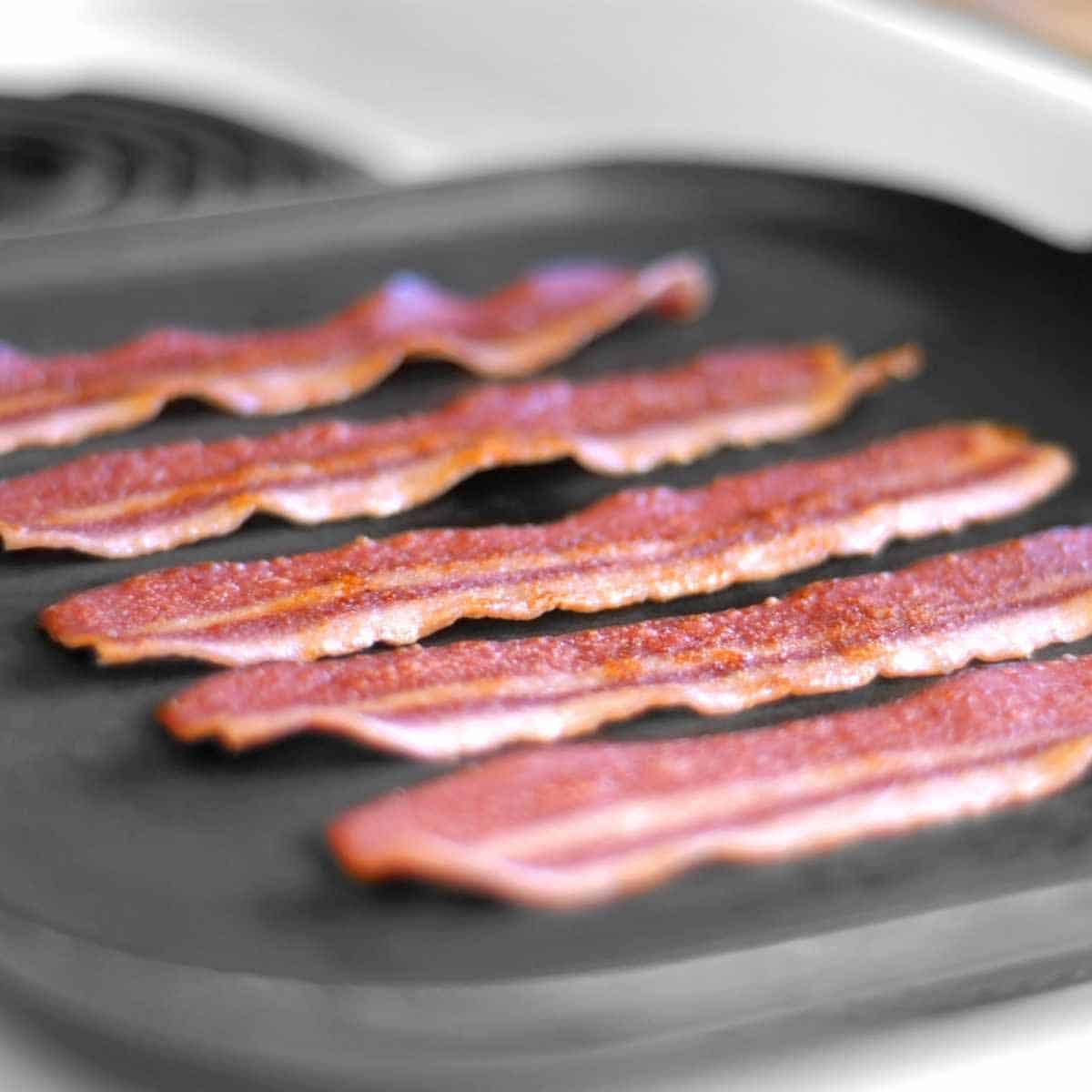 Five slices of turkey bacon reheated on a griddle.