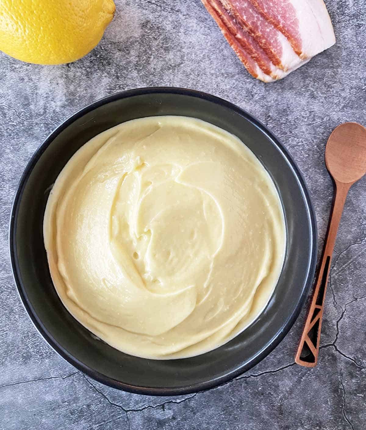 Bacon aioli spread in a black serving bowl with a wooden serving spoon nearby.