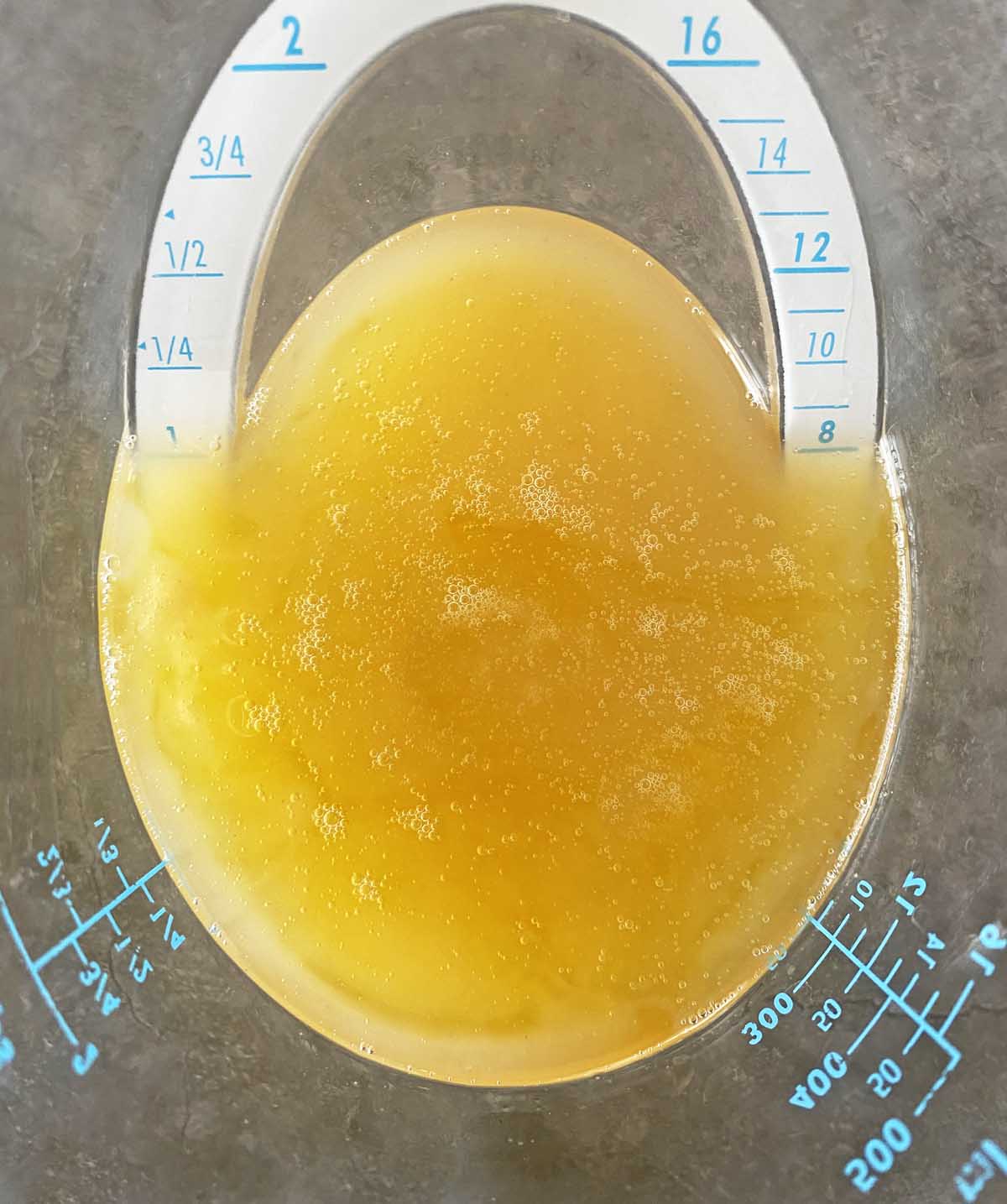 Close up of a measuring cup with half olive oil and half rendered bacon grease.