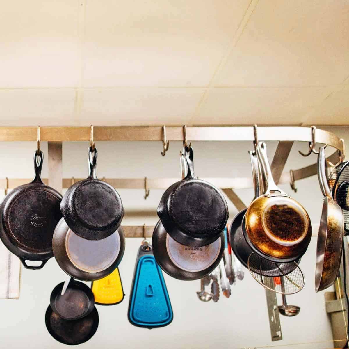 A ceiling mounted pot rack filled with 10 different frying pans and skillets.