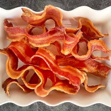 Cooked curly bacon piled in a white serving dish with wavy edges.