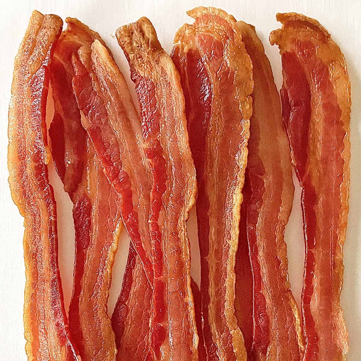Bacon frying in stove top pan. Sizzling bacon strips in silver skillet.  Stock Photo