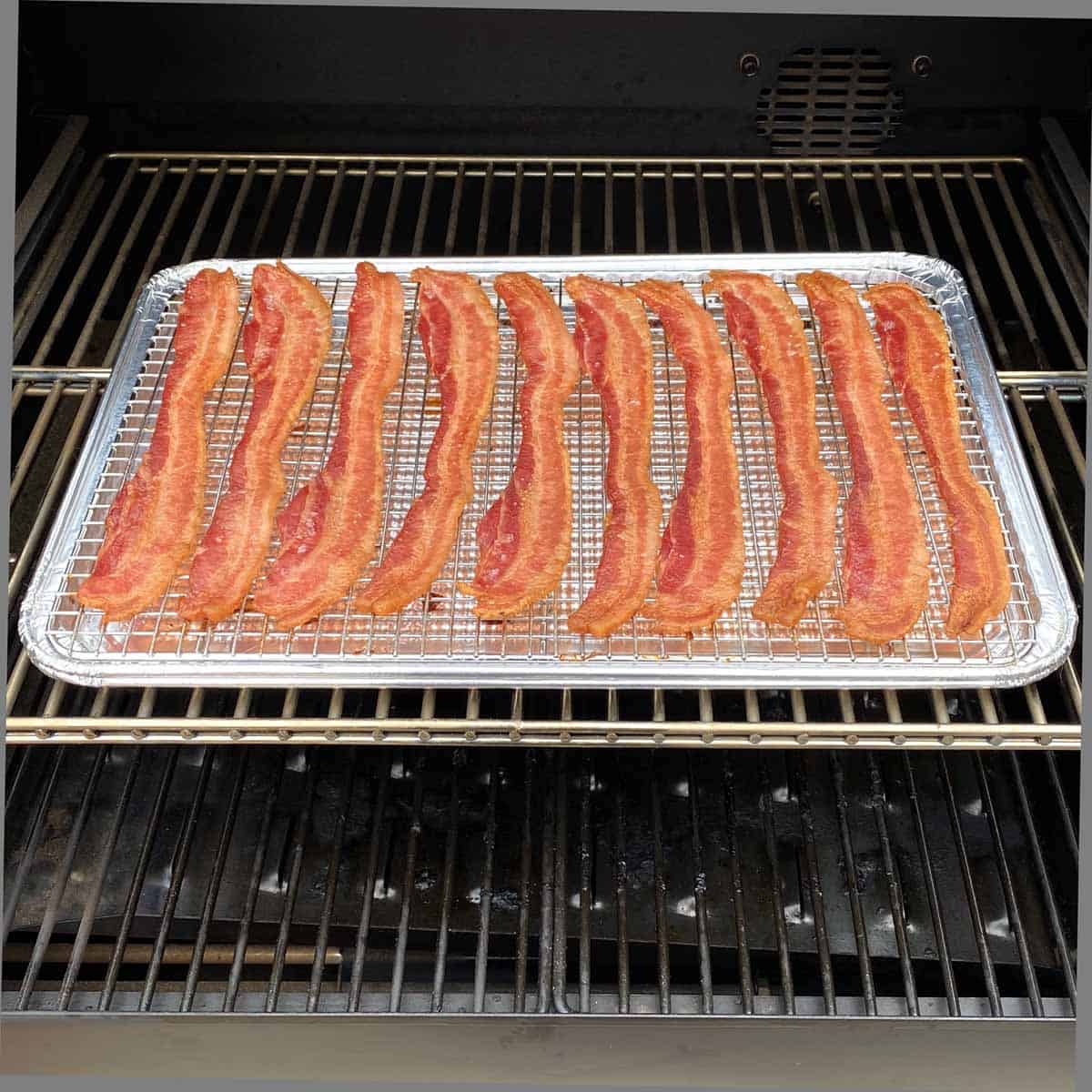 A pan of browned, cooked bacon on the middle rack inside a pellet grill.