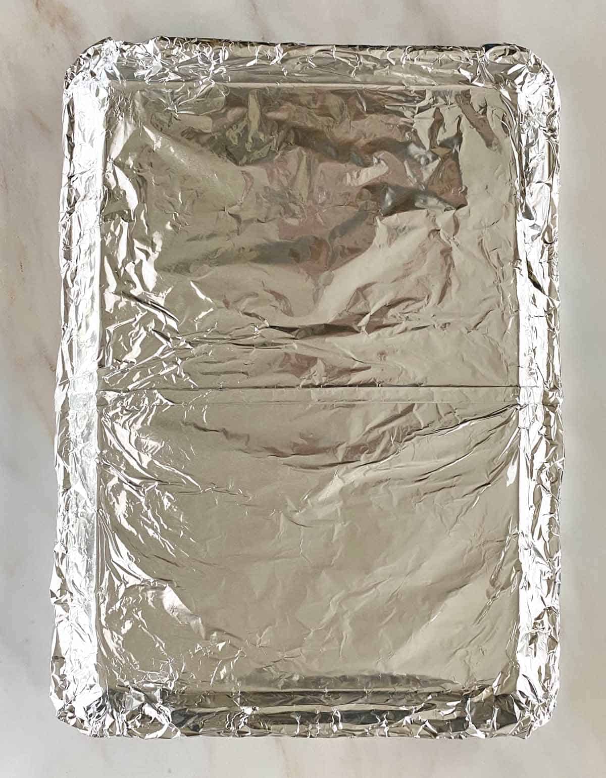 A baking sheet lined with aluminum foil, with a seam down the middle.