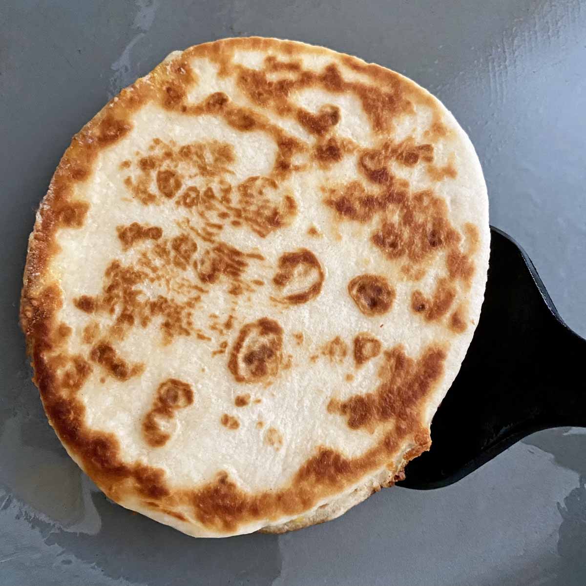 A mini quesadilla which has just been flipped over and is crispy and golden brown, in a hot frying pan.