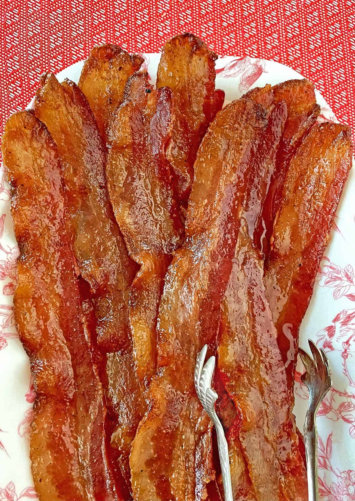 Ten strip of million dollar bacon piled on a pink and white serving dish with silver tongs.