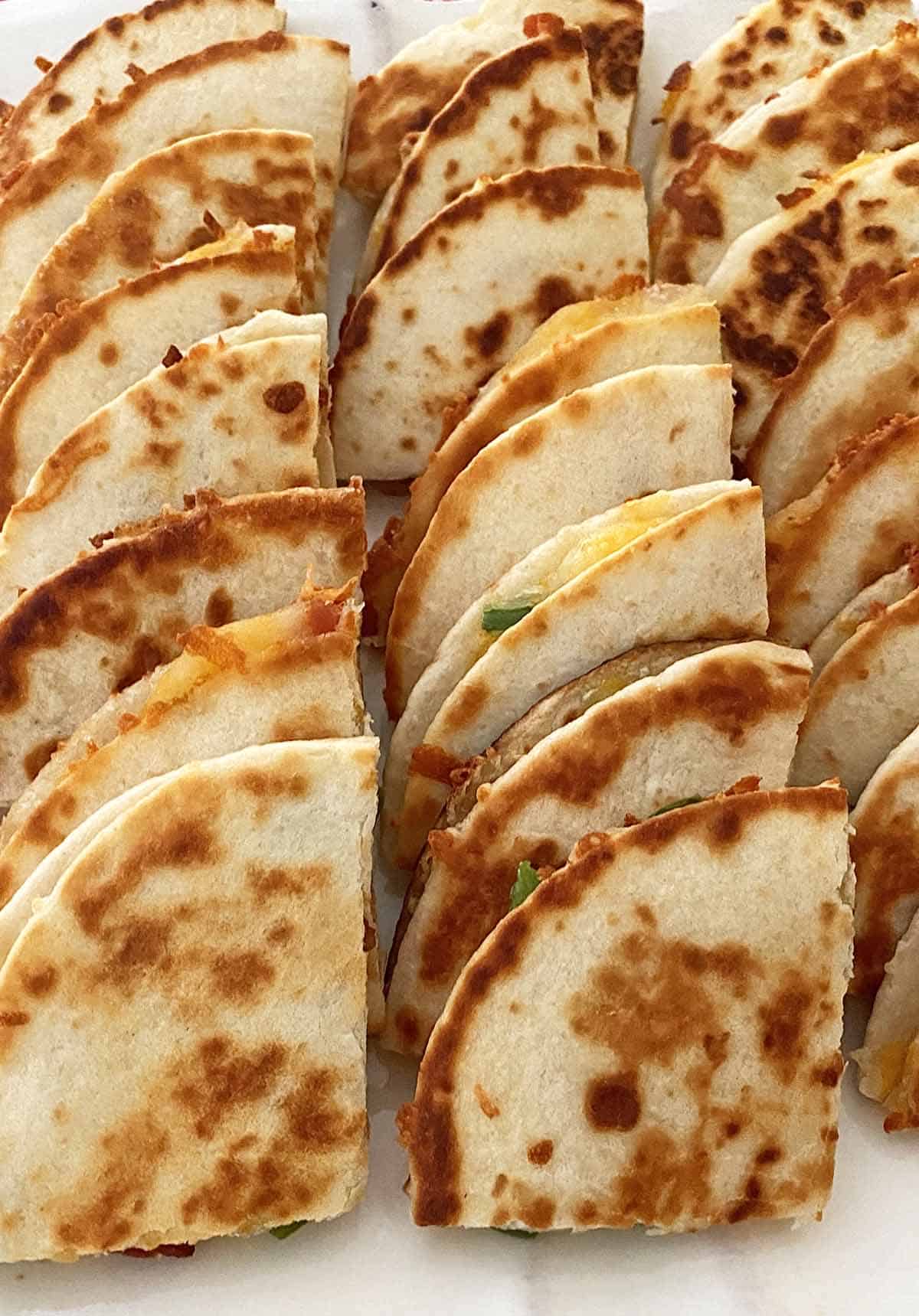 Two dozen quartered mini quesadillas arranged on a serving platter to serve as appetizers.