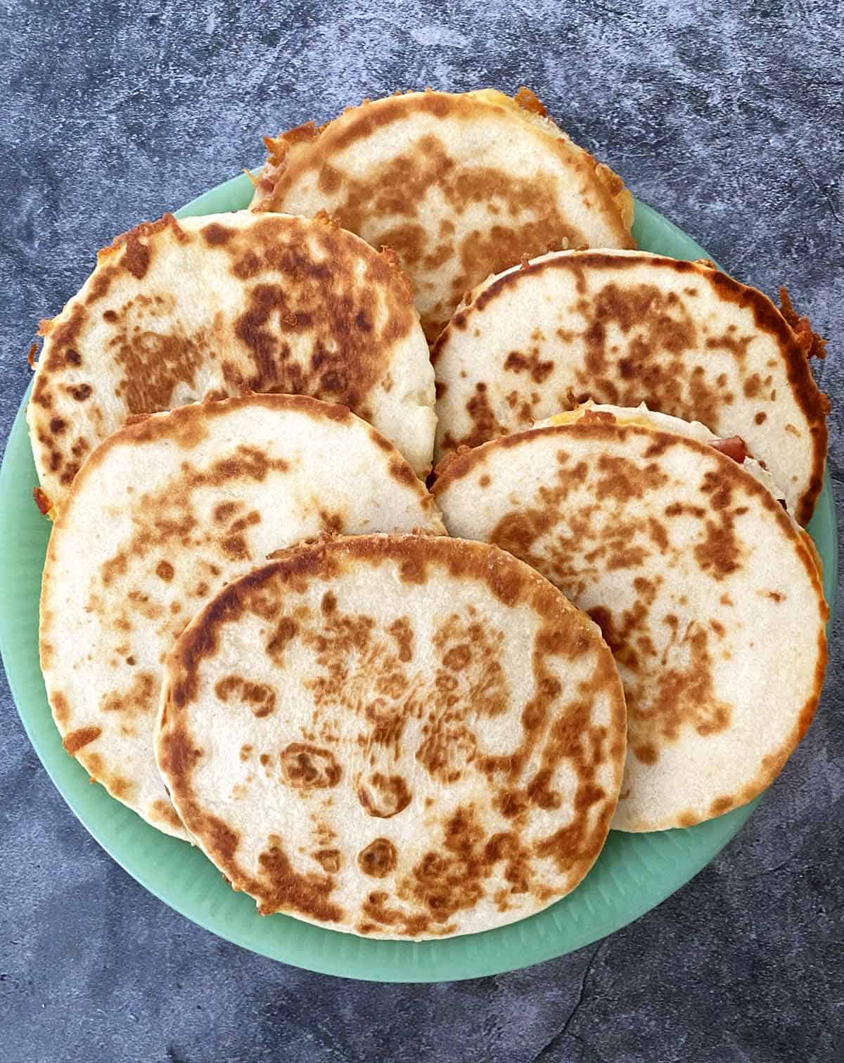 Six golden brown, just-cooked mini quesadillas on a green serving plate.