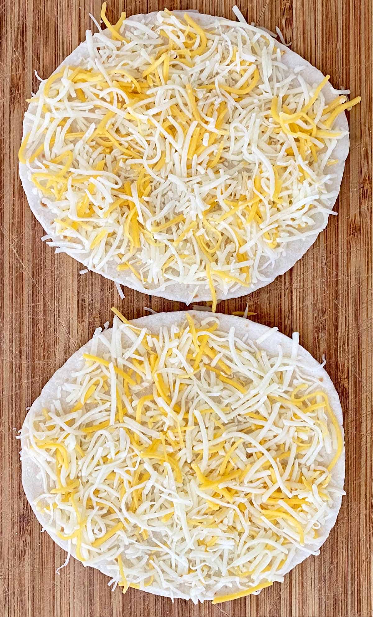Two mini flour tortillas sprinkled with shredded cheddar cheese.