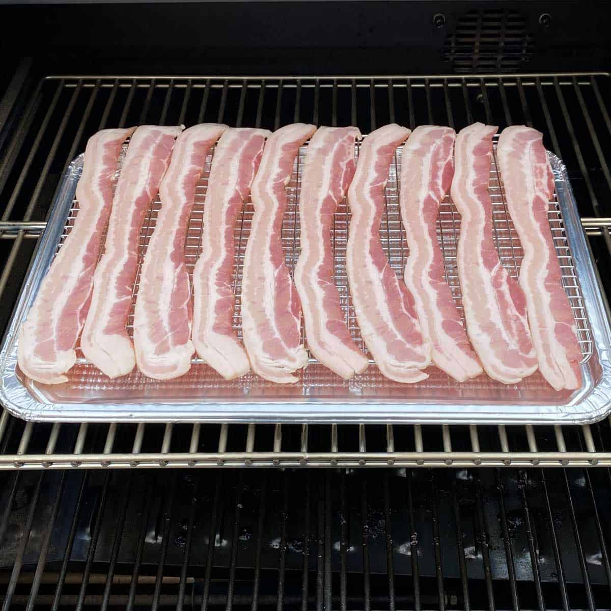 uncooked bacon on a foil baking sheet set inside a pellet smoker ready to be cooked.