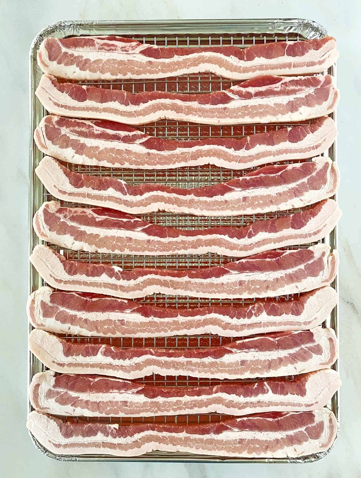 10 slices of thick cut bacon on a wire cooking rack set inside a disposable foil baking sheet.