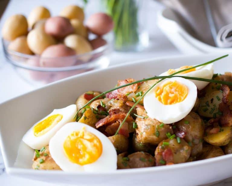 German Style Potato Salad in a white serving dish topped with soft boiled eggs.